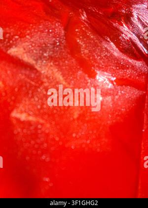Vue abstraite en gros plan d'un liquide rouge avec des glaçons. Les bulles et la condensation créent une texture. Couleurs vives et éclatantes adaptées aux rafraîchissements et aux célébrations Banque D'Images