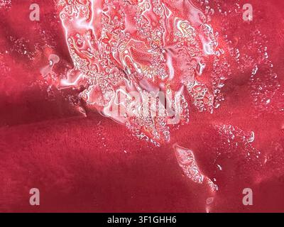Vue rapprochée abstraite d'un fond texturé rouge avec des gouttelettes liquides scintillantes. Détail de surface humide, texture brillante, prise de vue macro artistique, parfait pour Banque D'Images