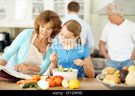 Lecture, recette et grand-mère avec enfant, cuisine et apprentissage des compétences culinaires dans la cuisine ou montrer. Femme âgée heureuse et préparation des repas avec une fille Banque D'Images
