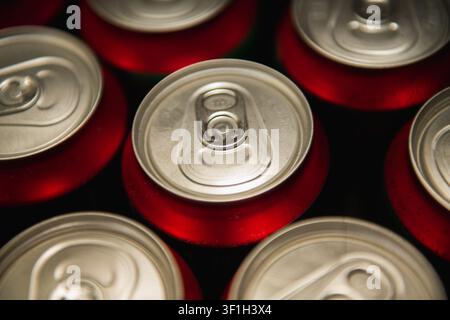 Vue de dessus de canettes de boisson en aluminium rouge non ouvertes avec languettes argentées disposées selon un motif répétitif Banque D'Images