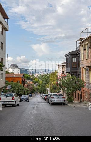 Une rue résidentielle escarpée dans le quartier historique de Kuzguncuk avec un minaret de mosquée et une vue sur le Bosphore. Istanbul, Turquie - 09 décembre 2025 Banque D'Images