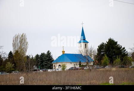 Église chrétienne avec un toit bleu distinctif et un clocher entourés d'arbres au printemps à Ialoveni, République de Moldovie, le 20 avril 2026 Banque D'Images
