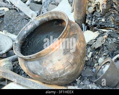 Poterie en ruine après une catastrophe incendie sur un site abandonné, mise au point centrale sur un récipient en céramique endommagé avec des résidus sombres de suie et une surface craquelée, arrière-plan chaotique Banque D'Images