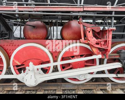 Vue détaillée d'un ensemble de roues de locomotive à vapeur vintage, composants mécaniques complexes, construction robuste, technologie ferroviaire du début du XXe siècle, peinture rouge w Banque D'Images