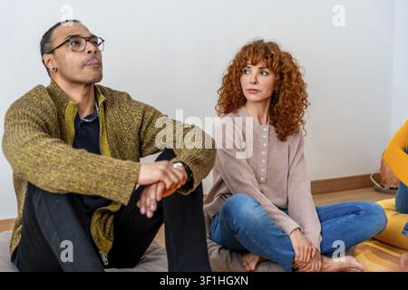 Différents adultes assis sur des coussins, écoutant et réfléchissant lors d'une séance de thérapie de groupe soutenue, favorisant le bien-être mental et la guérison émotionnelle Banque D'Images