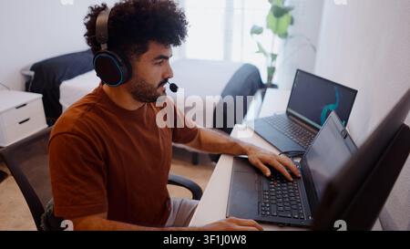 Jeune homme télétravailant depuis chez lui avec un casque, tapant sur un ordinateur portable Banque D'Images