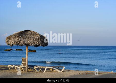 Transats vides sous des parasols en paille sur la plage de l'hôtel Meliá Trinidad Península, capturés en juillet 2026 à Trinidad, Cuba. Banque D'Images