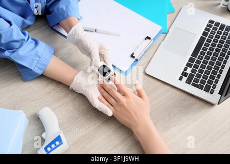 Professionnel médical en blouse bleue et gants blancs vérifiant la saturation en oxygène des patients avec un oxymètre de pouls Banque D'Images