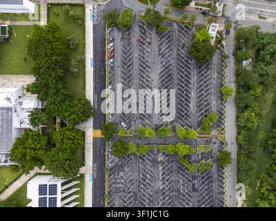 Vue aérienne d'un parking avec des places marquées, entouré d'arbres verts luxuriants et de bâtiments modernes dotés de panneaux solaires à Mérida, Yucatan, Mexique. Banque D'Images