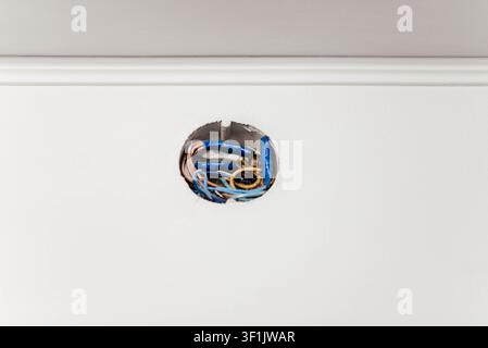 Close-up d'une boîte de jonction électrique ouverte avec câblage exposé à l'intérieur d'un mur blanc pendant la rénovation de la maison. Installation électrique, construction résidentielle, maintenance du câblage, réparation et concept de sécurité avec espace de copie. Banque D'Images