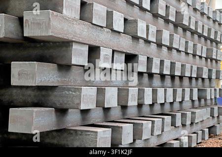 Cette photographie haute résolution capture les piles lourdes et texturées de billettes d'acier rectangulaires dans un entrepôt d'aciérie. L'image met en valeur le ra Banque D'Images