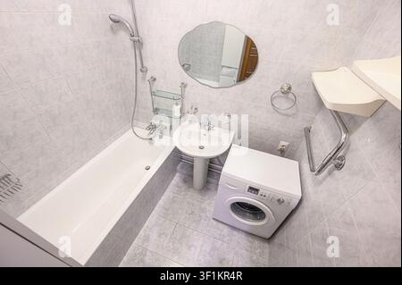 Plan large d'une salle de bains comportant une baignoire, un lavabo sur pied, une machine à laver et un miroir. La salle de bains est carrelée et dispose d'une disposition fonctionnelle Banque D'Images