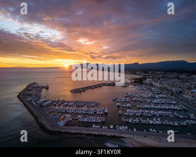 Vue aérienne d'une marina côtière au coucher du soleil, avec des rangées de yachts amarrés, une eau calme reflétant une lumière dorée, Espagne Banque D'Images
