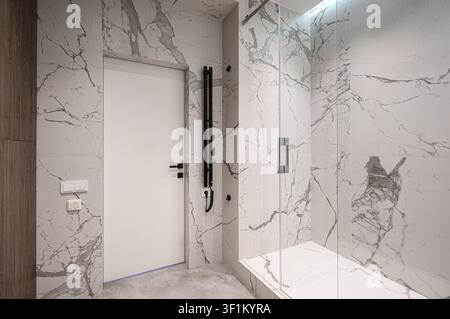 intérieur de salle de bain moderne avec murs en marbre, une douche vitrée et une porte blanche. Le design est épuré et contemporain Banque D'Images