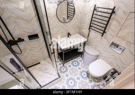 Une salle de bain moderne vue de dessus, avec des accessoires noirs, des carreaux motifs et du porcelaine blanc. L'espace compact comprend une douche, un lavabo, des toilettes et Banque D'Images