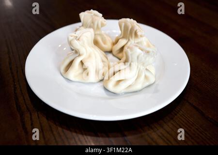 Dumplings khinkali géorgiens traditionnels, garniture savoureuse au poulet et au fromage, bouillon chaude à l'intérieur, servis dans une assiette en céramique blanche, cuisine faite à la main caucasienne Banque D'Images