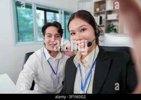 Agents de service client asiatiques souriants prenant un selfie dans un centre d'appels moderne Banque D'Images