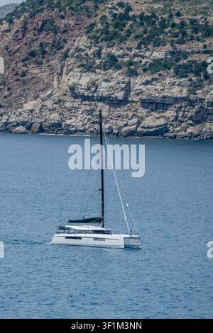 Catamaran de voile entrant dans la crique de Porto Ferro sur la côte méditerranéenne, photographié dans une lumière printanière vive près de Sassari, en Italie Banque D'Images