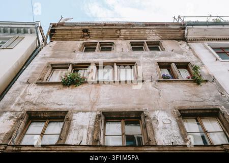 Un plan bas, pris de face, regardant vers le haut de la façade historique et érodée d'un vieux bâtiment européen, montrant plusieurs rangées de fenêtres en bois anciennes Banque D'Images