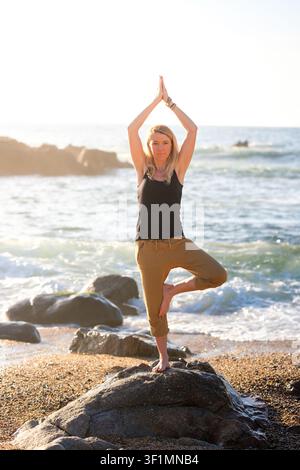 Femme en équilibre dans la pose de l'arbre du yoga, trouvant bien-être et pleine conscience sur une plage Banque D'Images