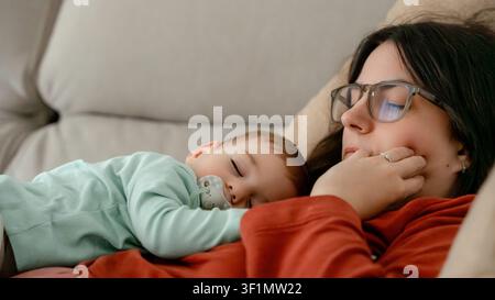 Une scène paisible d'une mère et d'un bébé reposant ensemble sur un canapé confortable, mettant en avant la chaleur et la connexion du temps de qualité en famille, avec le bébége Banque D'Images