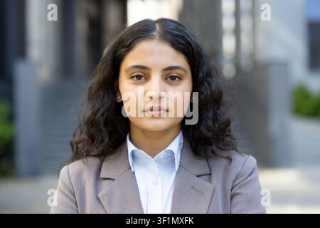 Jeune femme d'affaires debout avec assurance en plein air, portant un blazer sur mesure et une chemise bleu clair, incarnant le professionnalisme et le succès d'entreprise au cœur d'un environnement urbain Banque D'Images