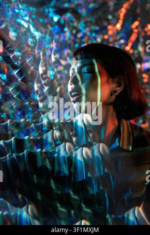 Jeune chanteuse latine interprétant les yeux fermés, capturée dans un effet de lentille kaléidoscopique vibrant. Des bokeh colorés et des réflexions prismatiques créent Banque D'Images