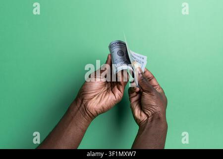 Close-up des mains d'un homme noir comptant et éparpillant des billets de dollar américain devant un fond vert propre, concept de paiement en espèces, budgétisation, épargne, i Banque D'Images