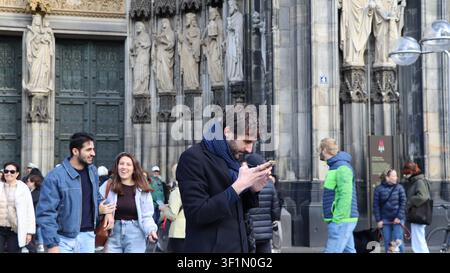 COLOGNE, ALLEMAGNE – 09.28.2024 : Des gens passent devant la cathédrale de Cologne et un homme regarde son smartphone Banque D'Images