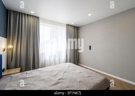 chambre à coucher douillette mettant en vedette un lit avec une couette à motifs géométriques, des rideaux gris encadrant une fenêtre lumineuse, et une ambiance chaleureuse et accueillante Banque D'Images