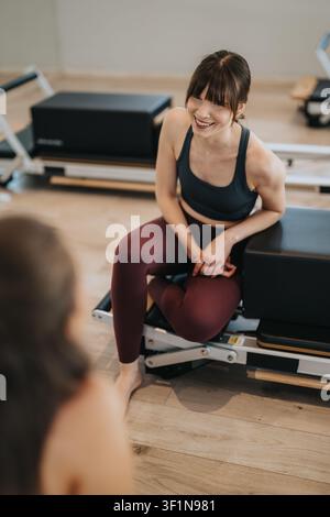 Femme souriante suivant un cours de Pilates Reformer avec une autre femme dans un studio lumineux Banque D'Images