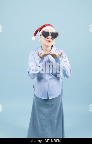 Jeune femme confuse portant un chapeau de Père Noël et des lunettes de soleil, regardant au loin dans le studio Banque D'Images