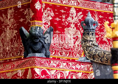 Statue de gardien en pierre noire sur un coin de temple décoré de rouge et d'or, montrant des motifs riches, des détails culturels et une architecture asiatique traditionnelle Banque D'Images