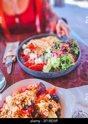 Une femme mange une salade avec une fourchette. La salade est dans une assiette et contient une variété de légumes, notamment de la laitue, des tomates et des concombres. La femme Banque D'Images