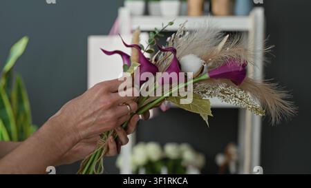 Femme fleuriste mains arranger le bouquet de calla violet avec l'herbe de pampas et l'eucalyptus et ficelle de cravate dans un studio ; artisanat calme. Banque D'Images