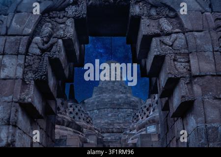 Stupa principale du temple de Borobudur à Java, en Indonésie, encadrée par des reliefs en pierre finement sculptés sous un ciel nocturne étoilé avec la Voie lactée visible au-dessus Banque D'Images