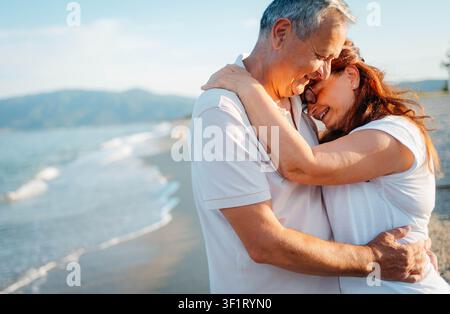 Couple de personnes âgées assis enlacées sur la plage Banque D'Images