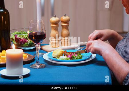 Une femme âgée savoure des aliments sains pendant le dîner lors d'un repas à la bougie, mettant l'accent sur le dîner romantique, les verres à vin et la table à manger dans le cadre d'une célébration en couple à la maison. Banque D'Images