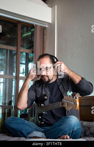 Bassist pensif portant des écouteurs avant de jouer de la basse électrique. Concept d'inspiration musicale, de préparation, de créativité, de concentration. Banque D'Images