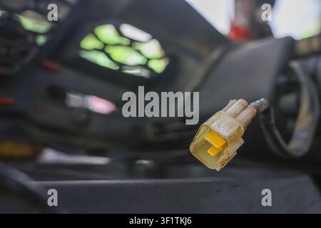 Un connecteur électrique en plastique jaune suspendu à un cadre de moto en fil de fer avec une faible profondeur de champ, gros plan montrant l'isolation usée et les bornes métalliques Banque D'Images