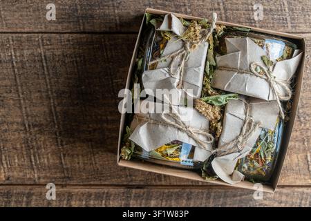 Quatre bocaux en verre avec fleurs sèches et tisane dans une boîte cadeau sur fond de bois, espace de copie, vue de dessus. Tisane Banque D'Images