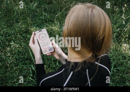 Femme assise sur l'herbe tenant un smartphone affichant une application de suivi des hormones. entraînement de synchronisation du cycle, application de cycle menstruel, suivi femtech, femmes Banque D'Images