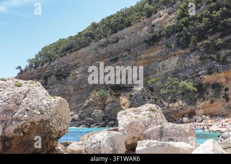 Vue de Cala Mariolu avec de gros blocs de calcaire blanc, une mer turquoise et des falaises rocheuses abruptes couvertes de broussailles méditerranéennes à Baunei, Sardaigne, It Banque D'Images
