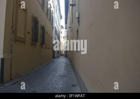 Ruelle pavée étroite et ombragée entre des bâtiments historiques à Florence, en Italie, menant vers une rue ensoleillée au loin Banque D'Images