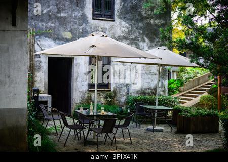 Un espace de détente extérieur avec des tables, des chaises et des parasols devant un vieux bâtiment. Banque D'Images