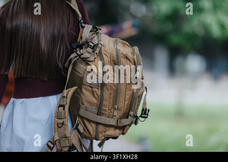 Élève du lycée vu de dos portant un grand sac à dos beige en marchant à l'extérieur sur le campus Banque D'Images