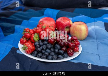 Un plan rapproché horizontal à hauteur élevée d'une assiette blanche remplie à ras bord de fraises fraîches mûres, de myrtilles et de cerises sucrées, placée à côté t Banque D'Images