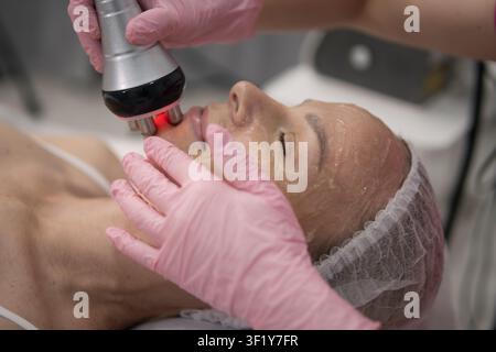 Femme soumise à un traitement facial par radiofréquence non invasif avec un appareil spécialisé, visant le raffermissement de la peau et le rajeunissement juvénile dans un p Banque D'Images
