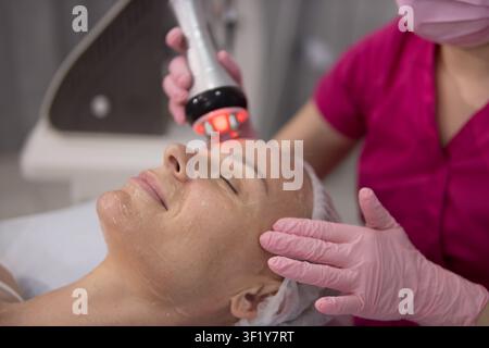 Femme soumise à un lifting par radiofréquence sur son visage avec un appareil spécialisé, recherchant un raffermissement et une revitalisation cutanée par un cosmétologue professionnel Banque D'Images