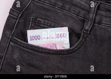 Billet de monnaie ukrainien dépassant d'une poche de jean noir, texture denim sombre, détail de poche ouverte, concept financier, style décontracté, arrière-plan minimal Banque D'Images